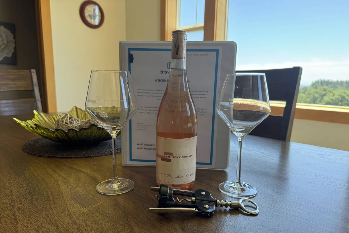 A welcoming interior vignette featuring a chilled bottle of estate rosé, two elegant wine glasses, a handwritten welcome note, a corkscrew, and a decorative bowl arranged on a table by a window. The soft natural light and thoughtful presentation convey a sense of arrival and hospitality.