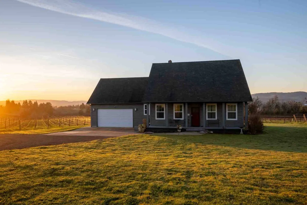 This exterior shot captures the farmhouse at sunset, with a welcoming front porch and the tranquil countryside surrounding the home. The warm glow of dusk highlights the peaceful setting, and the porch is clearly a space for relaxation and enjoying the views. Open land and the presence of vineyards or fields in the background evoke the region’s rural beauty.