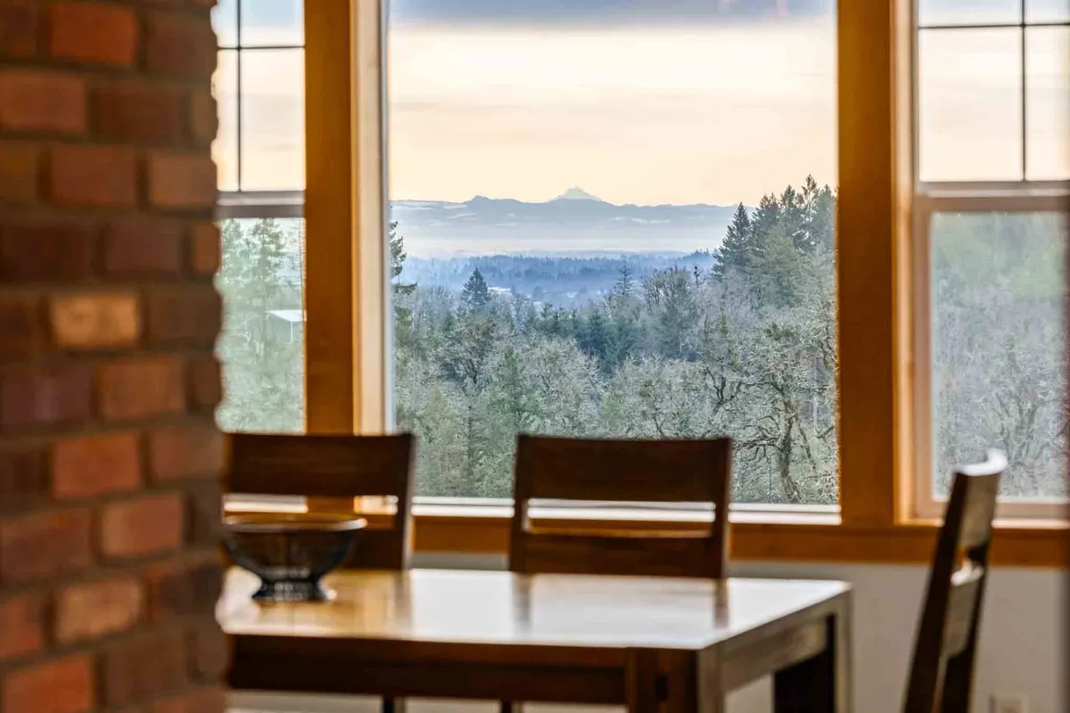A serene dining space with a large wooden table set before expansive windows that open to mountain views. The room is filled with natural light, perfect for morning coffee or family meals, and invites quiet moments of reflection.